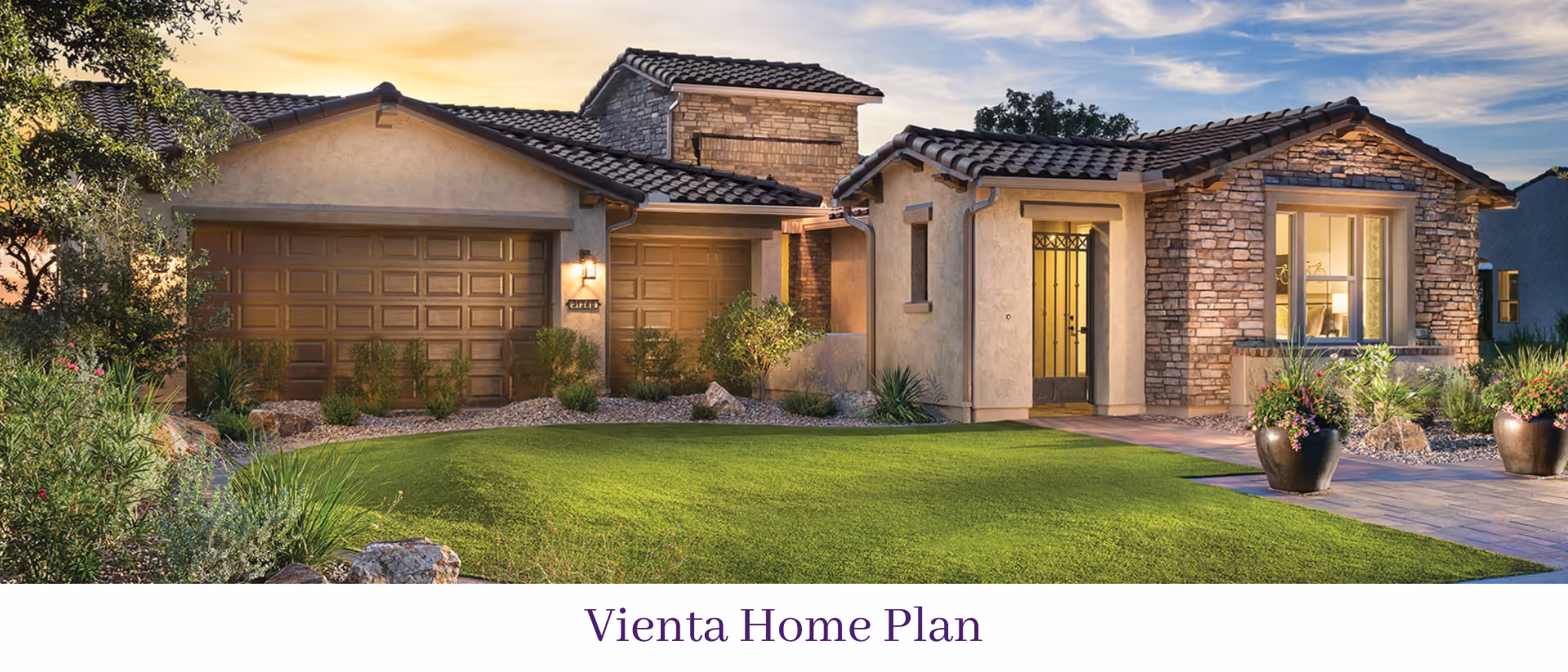 Exterior view of a single-story house with a two-car garage, stone and stucco facade, tiled roof, and a well-maintained green lawn with plants and shrubs. The house is shown during sunset or early evening with warm lighting.