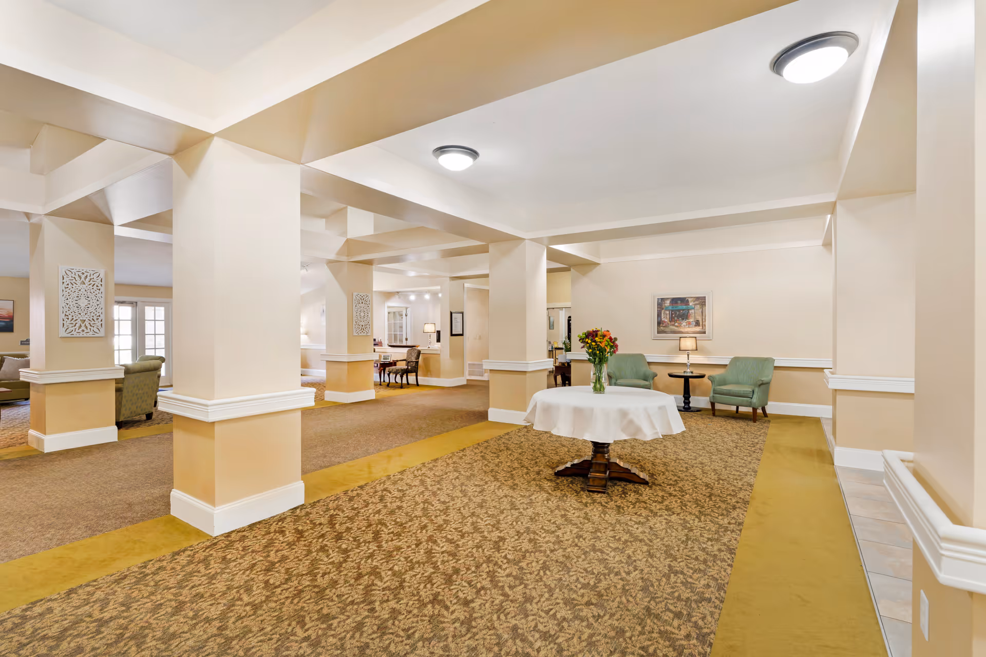 Spacious senior living facility common area with pillars, a round table topped with flowers, and seating arrangements.