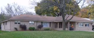 Single-story beige assisted living building with a front lawn and tall trees.