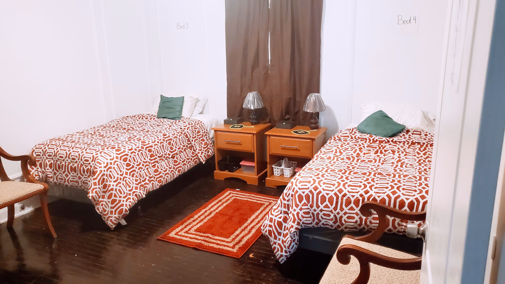 Shared bedroom with two single beds, matching patterned bedspreads, bedside tables with lamps, and chairs.