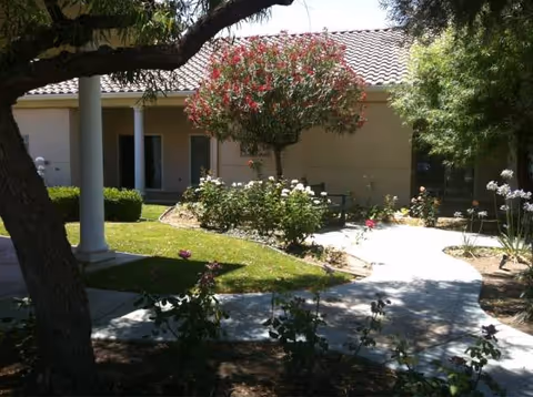 Front exterior of a senior living facility with a landscaped courtyard and walkway.