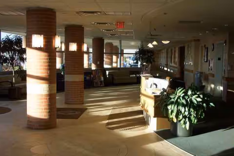 Sunlit interior lobby with brick columns, reception desk, seating, and potted plants.