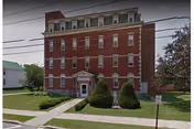 Exterior view of a red brick, multi-story building with a manicured lawn and front entrance.