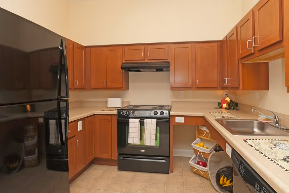 Kitchen with cherry wood cabinets, black refrigerator and stove, beige countertops and a stainless steel sink.