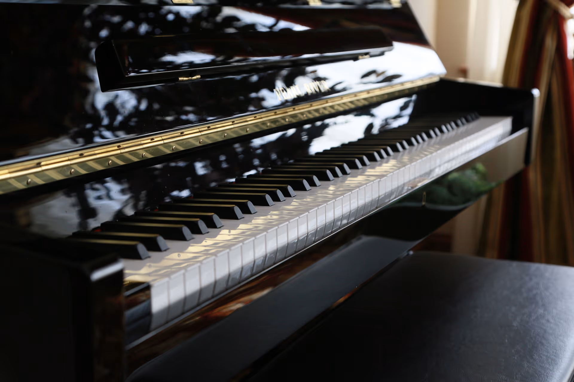 Close-up of a glossy black piano keyboard and bench in a softly lit interior.