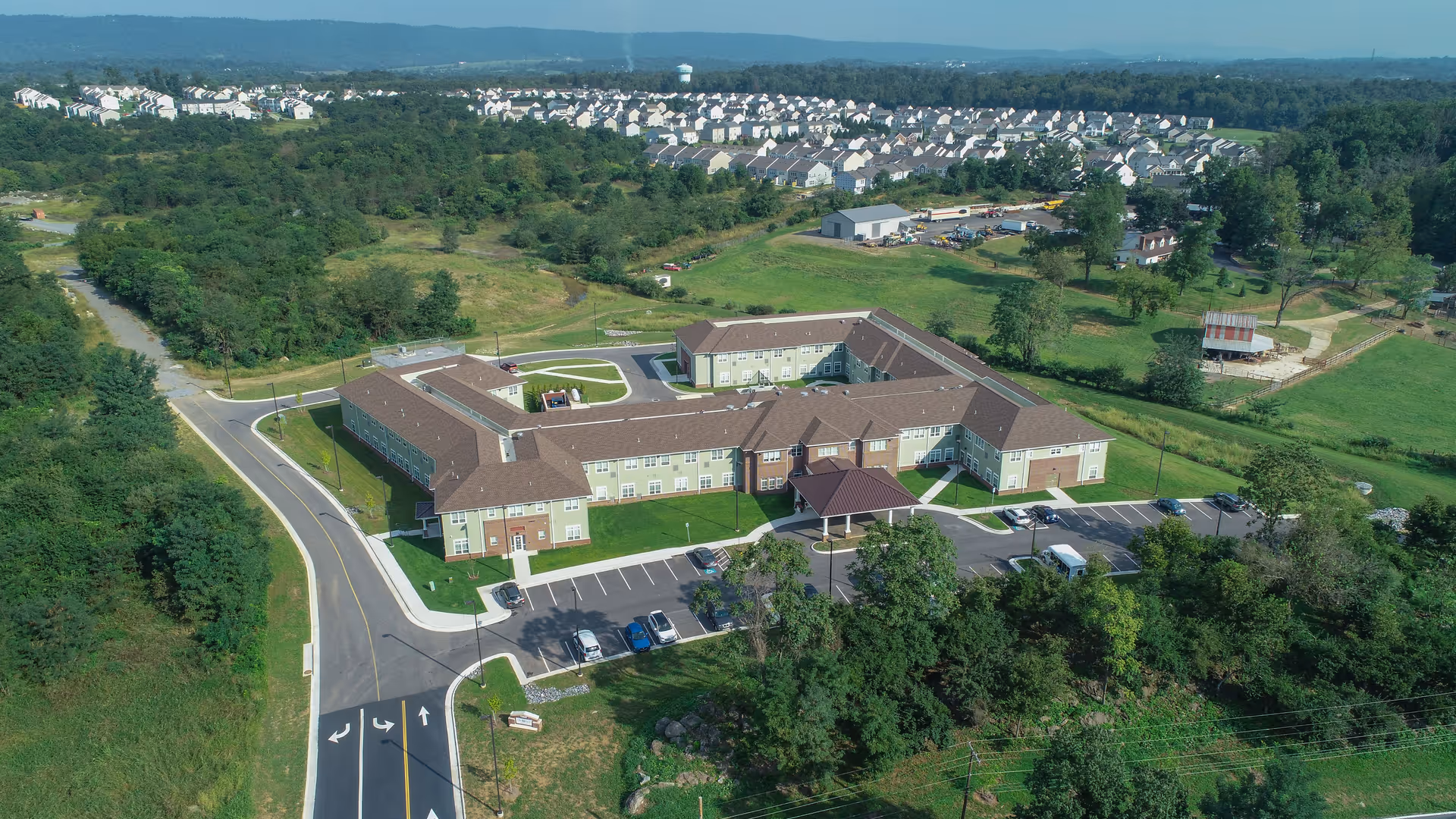 Aerial view of the Harmony at Martinsburg senior living facility building with surrounding parking lot, roads, and green landscape.