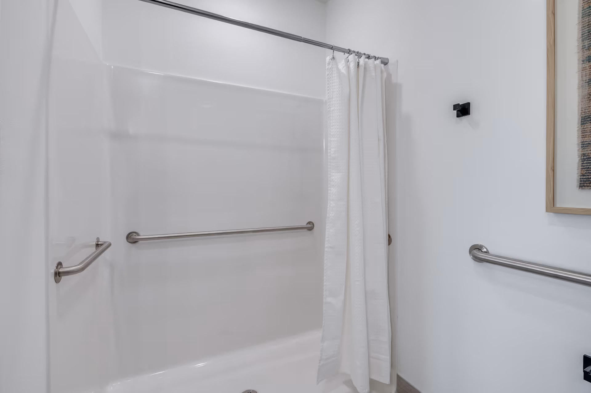 Accessible white bathtub-shower with a white curtain and stainless steel grab bars on white walls.