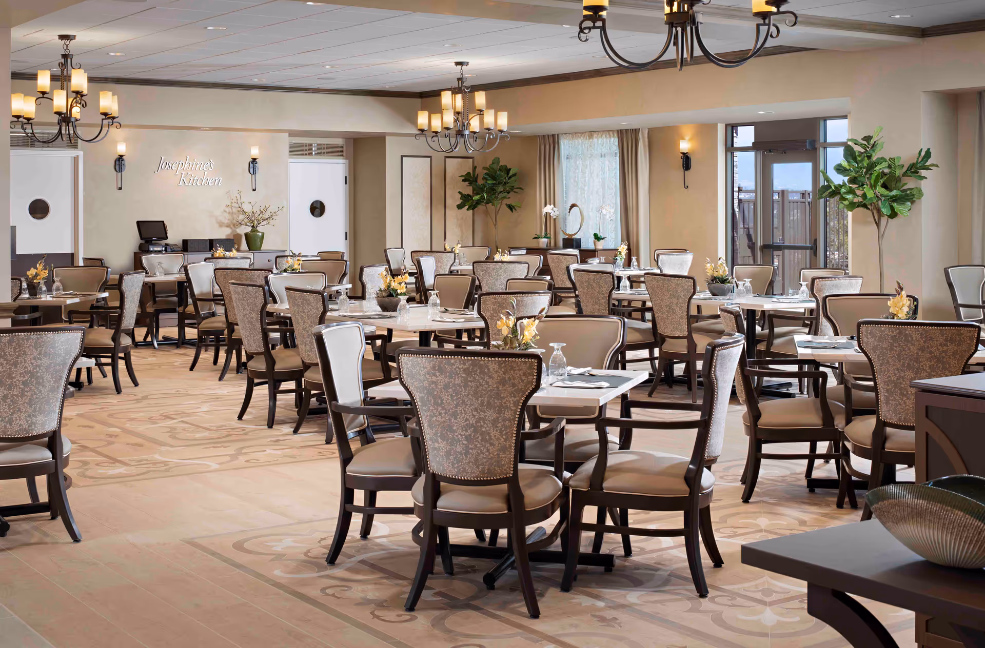 Bright, elegant senior living dining room with multiple set tables and upholstered chairs.