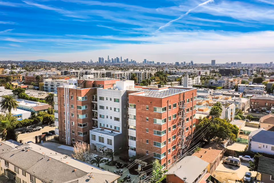 Aerial view of a multi-story senior living facility building in an urban area with a clear blue sky and city skyline in the background.