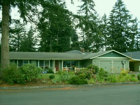 Front view of a single-story home with a garden and tall trees behind.