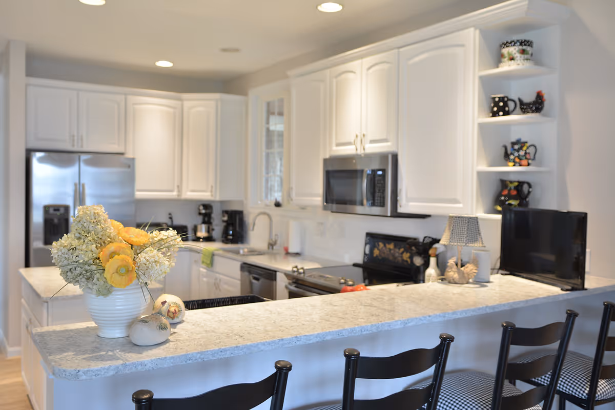 Bright modern kitchen with white cabinets, stainless appliances, a marble countertop island with bar stools and a vase of flowers.