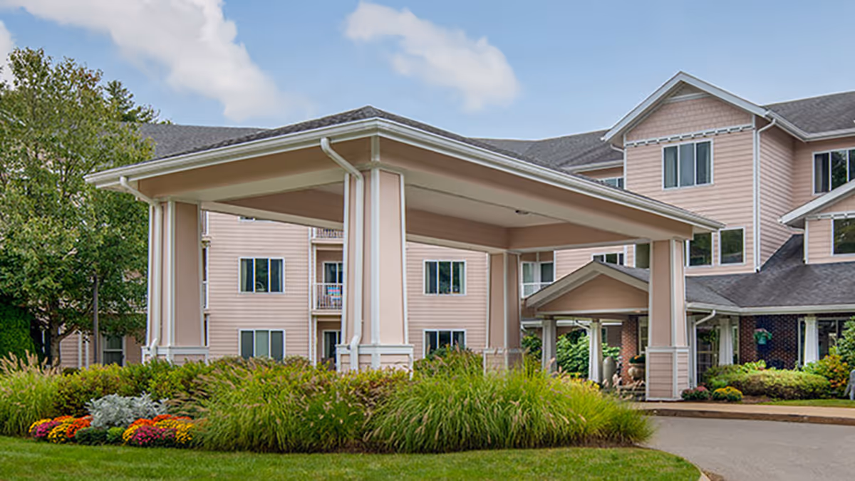 Covered porte-cochere entrance of a multi-story pink senior living building with manicured landscaping.