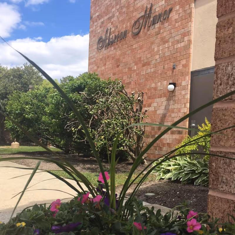 Exterior brick facade of Absecon Manor Nursing Home with plants and walkway.