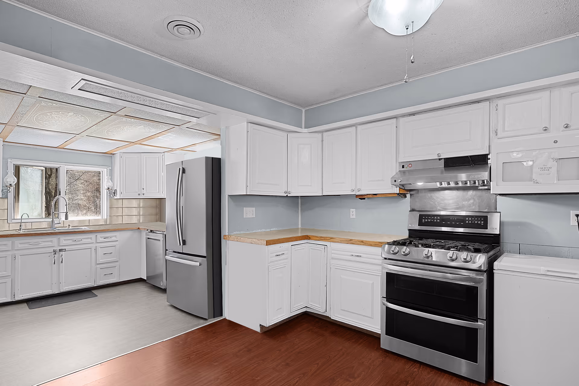 Spacious kitchen with white cabinets, wood countertops, a stainless steel refrigerator and gas range, and a sink beneath a window.