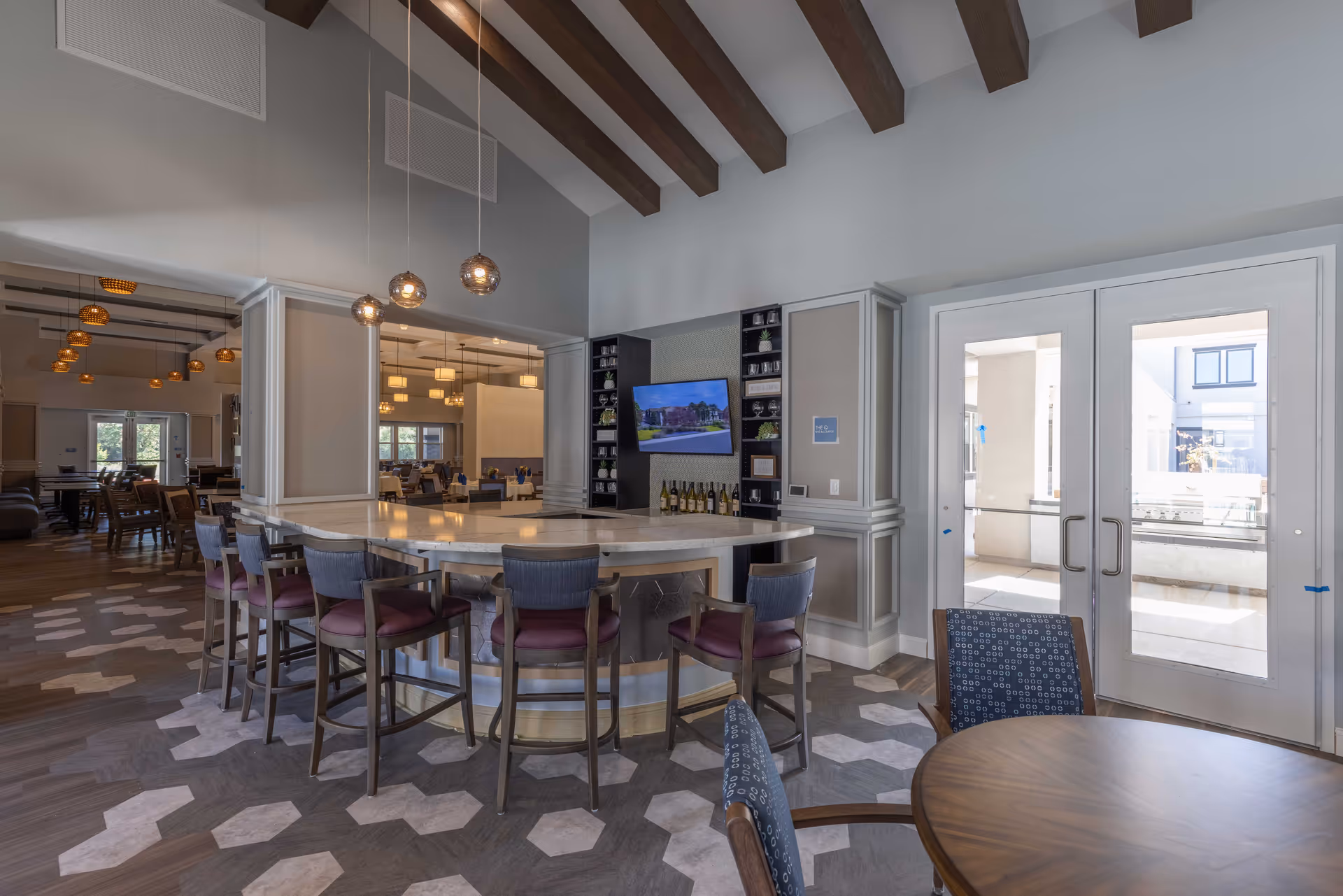 Spacious community dining and lounge area with a curved bar, high chairs, tables, and exposed ceiling beams.