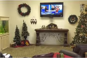 Decorated common room with a mounted TV, festive wreaths and Christmas trees, an ornate console table, an aquarium, and seating.