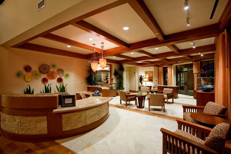 Warmly lit reception lobby with a curved front desk, seating area of armchairs and tables, decorative wall art and pendant lights.