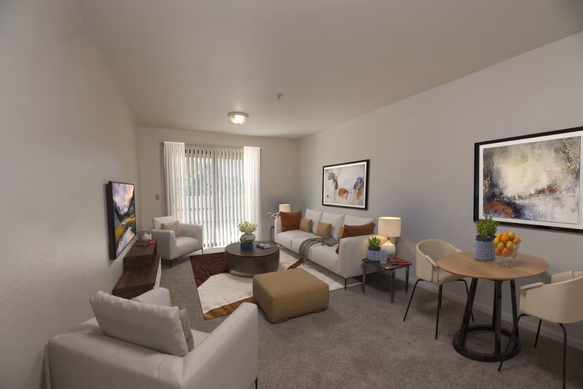 A cozy senior living room with beige walls and carpet. The room features a white sofa with brown and beige cushions, two white armchairs, a brown ottoman, and a round coffee table with a flower arrangement. There is a small round dining table with three chairs, a bowl of oranges, and a potted plant. Two abstract paintings hang on the walls, and a flat-screen TV is mounted on the wall opposite the sofa. Vertical blinds cover a sliding glass door that lets in natural light.