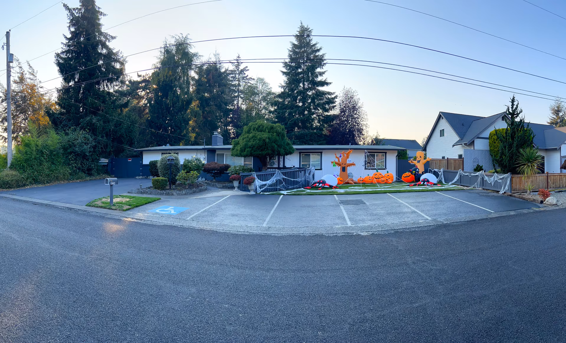 Single-story senior care home building with a small parking lot and Halloween decorations (inflatable pumpkins and ghosts) in front, framed by trees.