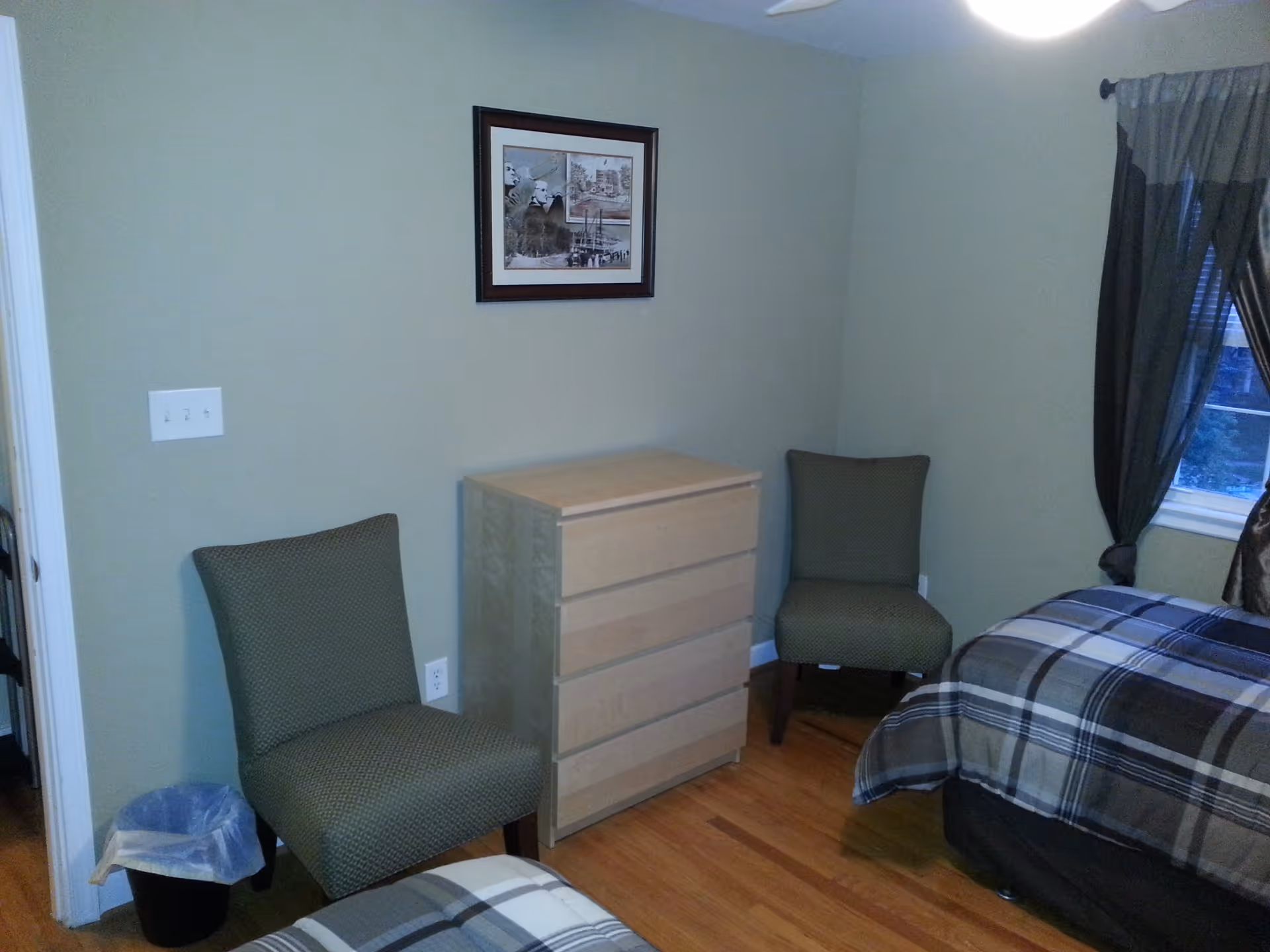 Small bedroom with two chairs, a light wood dresser, and twin beds with plaid bedding.