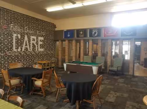 Recreation/lounge interior with a pool table, round tables and chairs, and a brick wall mural reading 'CARE'.