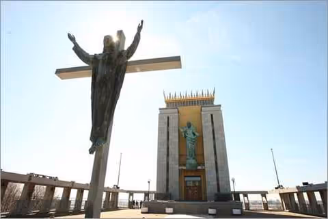 Outdoor view of a tall building with a statue and a large crucifix in foreground.