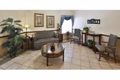 A tiled-floor sitting area with a sofa, armchairs, a round coffee table, plants, and wall decorations.