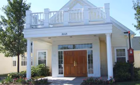 Front view of a light-colored senior housing building with a double wooden door entrance and balcony.