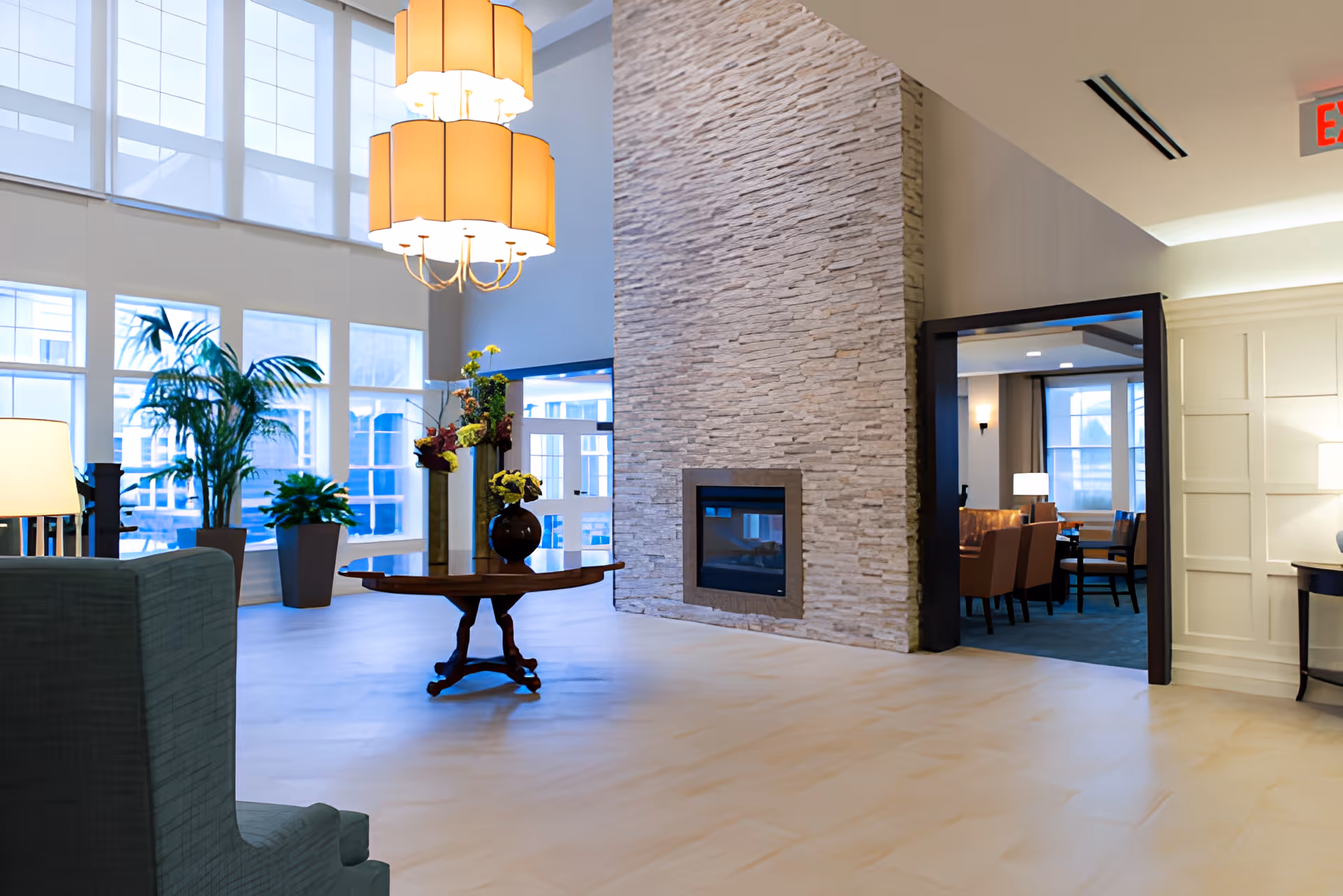 Spacious, well-lit lobby with a round centerpiece table, stone fireplace, tall windows, and seating.