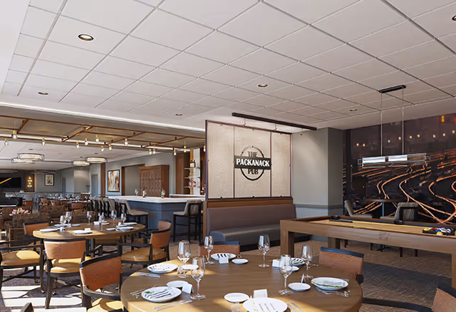 Interior view of a senior living facility's dining and recreational area featuring round dining tables set with plates, glasses, and napkins, a bar with stools, a pool table, and a sign that reads 'The Packanack Pub'. The room has a modern ceiling with recessed lighting and large windows allowing natural light.