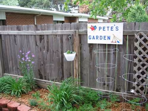 Wooden fence garden area with hanging planter, circular plant supports, and Pete's Garden sign.