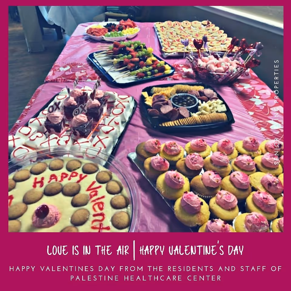 A pink-covered table filled with Valentine's Day desserts—cupcakes, cookies, and fruit skewers—with a festive magenta greeting border.