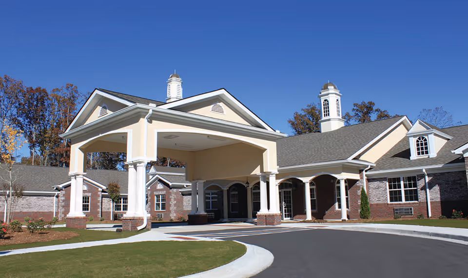 Exterior view of Benton House of Sugar Hill, showing a large covered entrance with columns, brick and beige siding, multiple windows, and a clear blue sky.