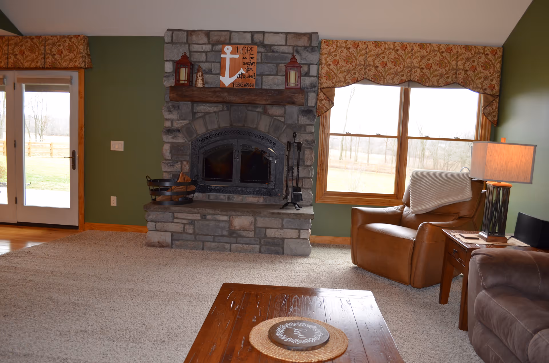 Cozy living room with a stone fireplace, leather armchair, large window, and wooden coffee table.