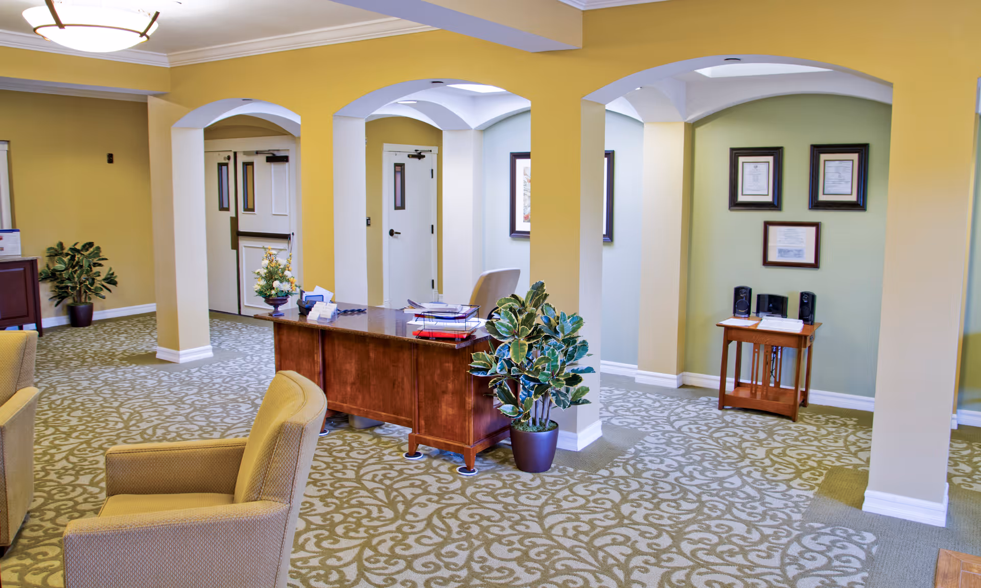 Reception lobby with a wooden desk, seating, potted plants and arched columns.