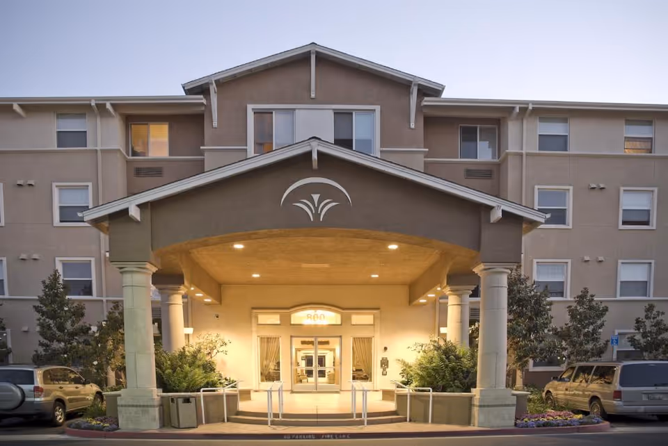 Front entrance with a covered porte-cochère of a multi-story senior living building lit at dusk.