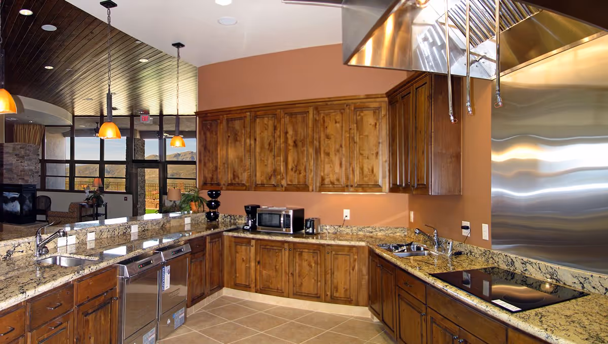 Open communal kitchen with wooden cabinetry, granite countertops, stainless appliances, and pendant lights overlooking a seating area.