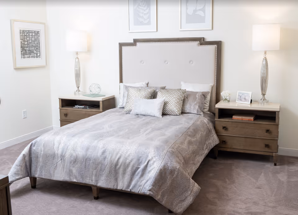 Well-lit bedroom with an upholstered headboard, a made bed with decorative pillows and matching nightstands and lamps.