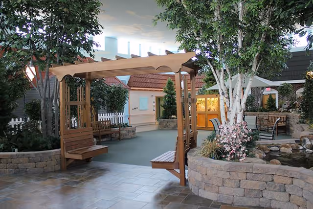 Indoor courtyard with a wooden pergola and swinging benches surrounded by trees, seating areas, and a small pond.
