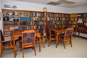 Interior library/reading room at Pinecrest Manor with wooden tables, chairs, and tall bookshelves.