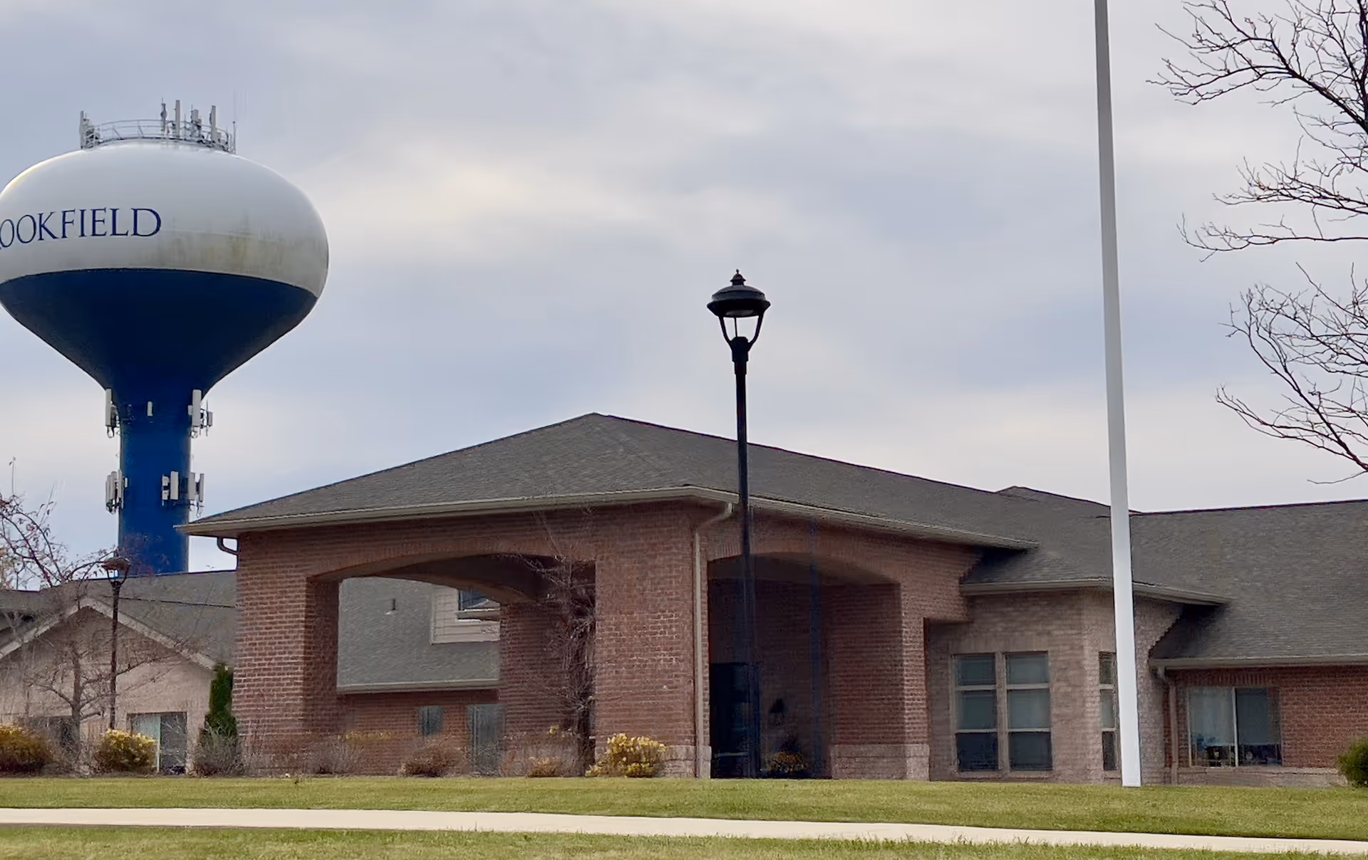 Single-story brick assisted living building with a covered entrance and a water tower visible behind it.