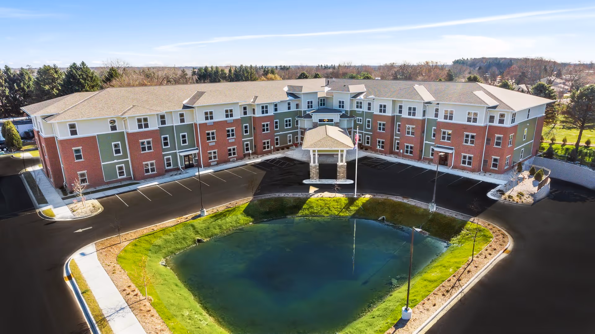 Aerial view of a three-story senior living building with a circular driveway and pond in front.