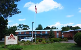 Front exterior of a single-story brick senior living facility with a flagpole and parked cars.