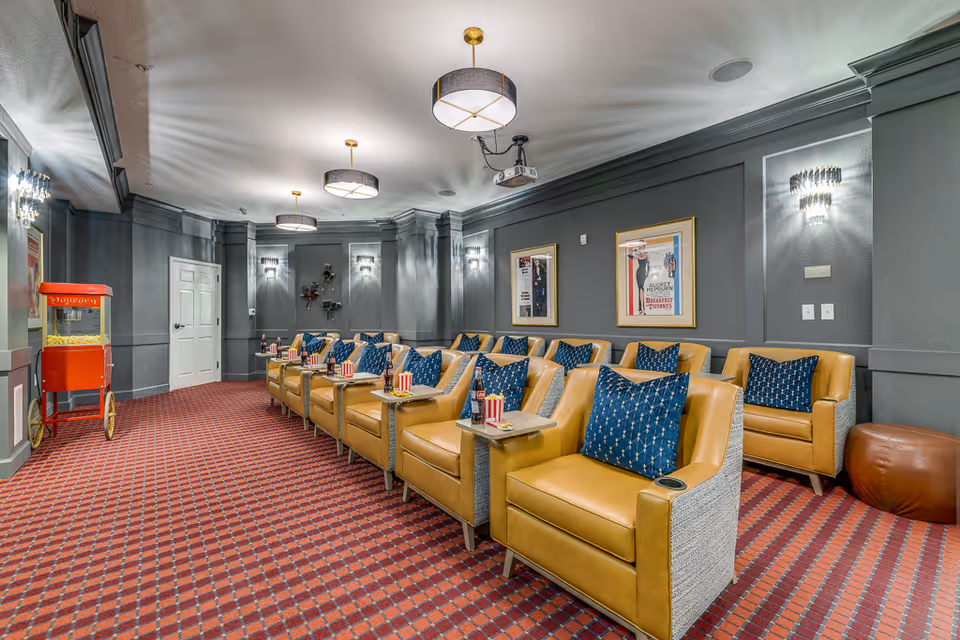 A cozy resident theater room with rows of leather recliners, blue pillows, a popcorn machine, and a ceiling projector.