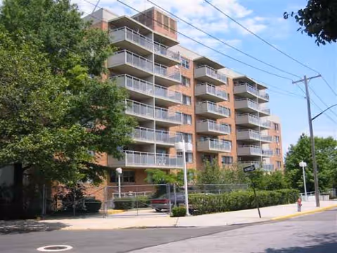 Exterior view of a multi-story brick senior living building with balconies and surrounding trees.