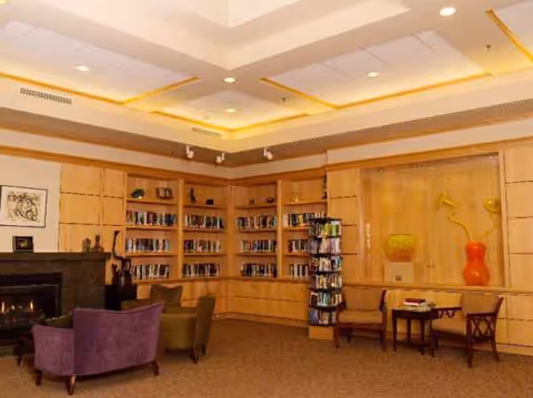 A cozy senior living lounge at The Summit at First Hill with bookshelves and fireplace.