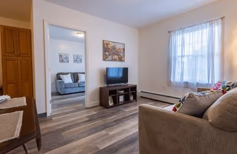 Living room with a sofa, TV on a stand, large window, and a doorway to an adjacent room.
