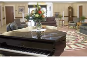 Elegant living room with grand piano, floral bouquet, and plush seating around a patterned rug.