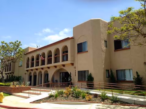 Exterior view of a tan, arched, multi-story senior living building with landscaping.