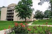 Exterior view of a multi-story senior living building with balconies, a lawn, pathways, and flowering shrubs.